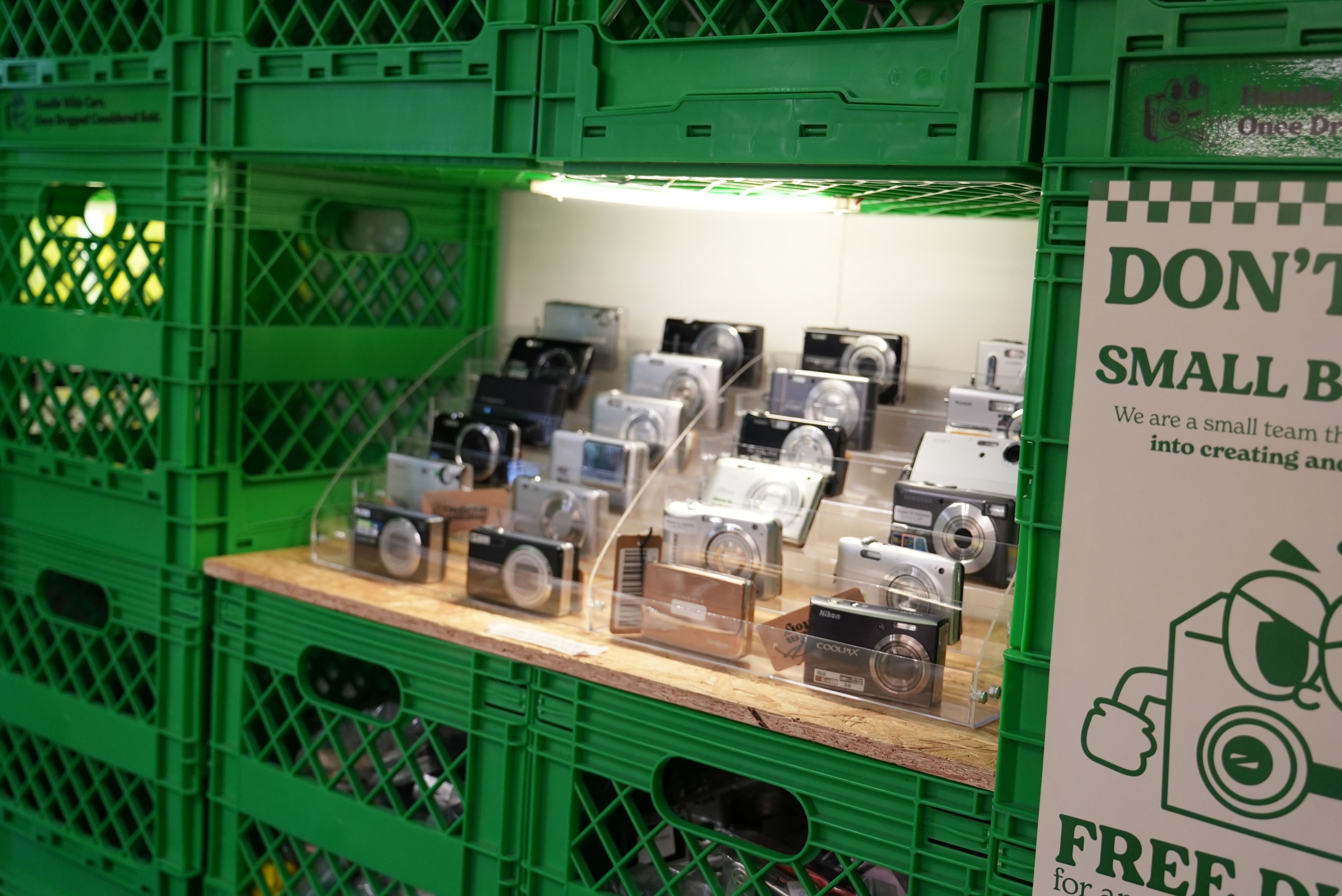 A display of digital cameras stand in the gap between crates. Photo: Stella McGann.